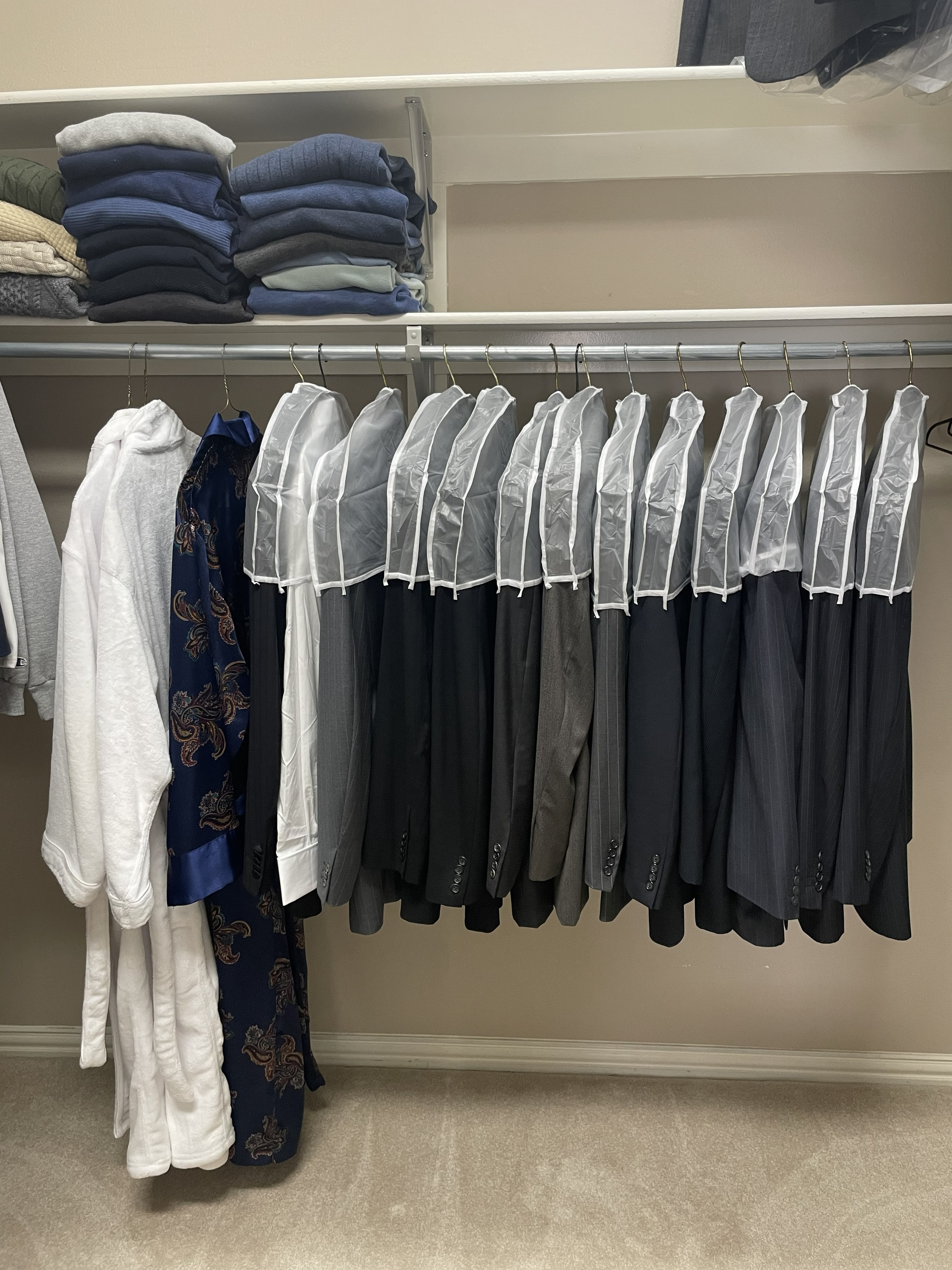 Suits in garment bags hanging neatly in organized closet